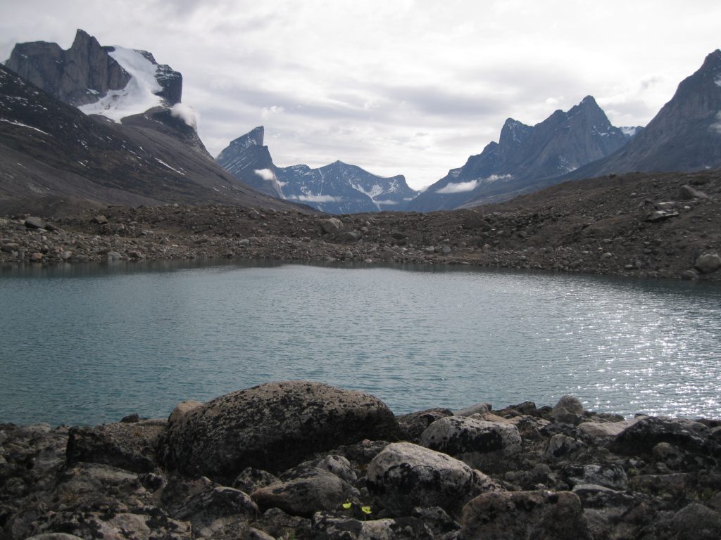 Breidablik Peak to the left, Mount Thor in the centre, Mount Northumbria to the right fronted by a small lake, boulders and two arctic poppy flowers at Summit Lake